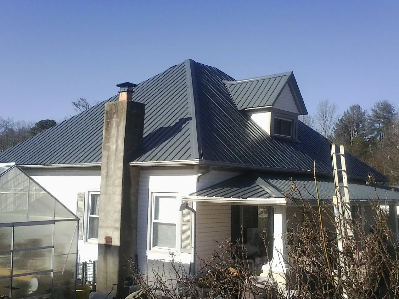 Dark blue standing seam metal roof on a white farmhouse with dormer — Slate & Tile Roof Repair by Roofing Brothers in Harlem