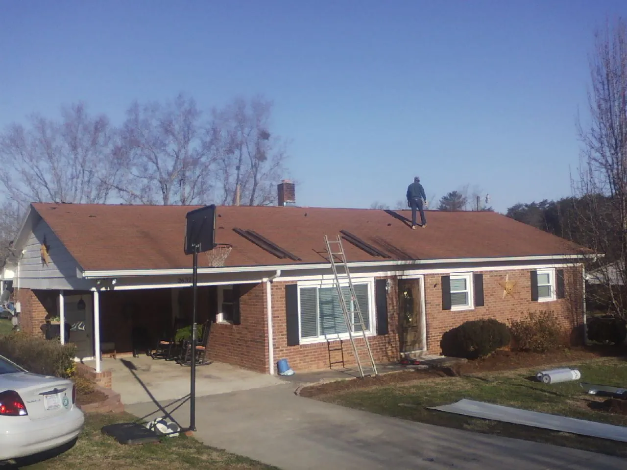 Roofer stripping a shingle roof on a brick ranch before metal panels in Harlem