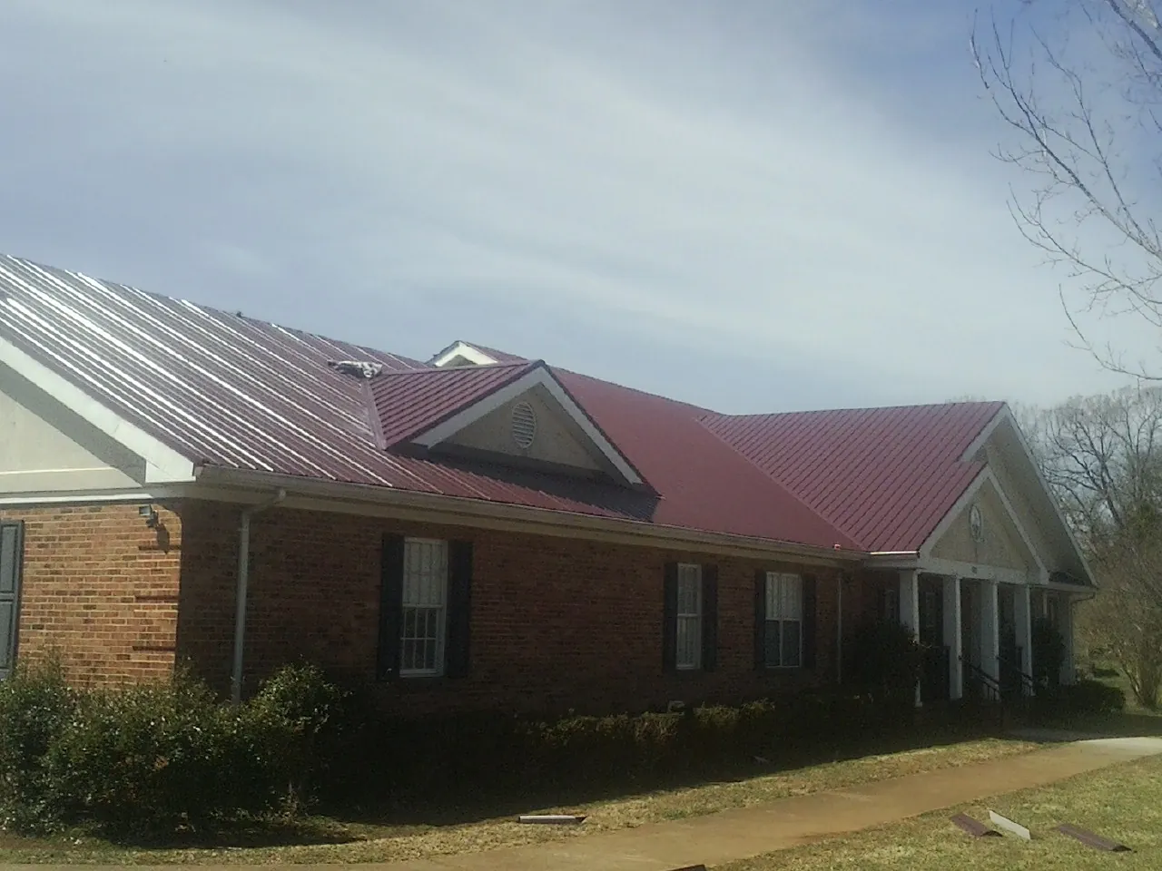 Red metal roof with gabled entries on a long brick building, from a Hail Damage Roof Repair job in Harlem