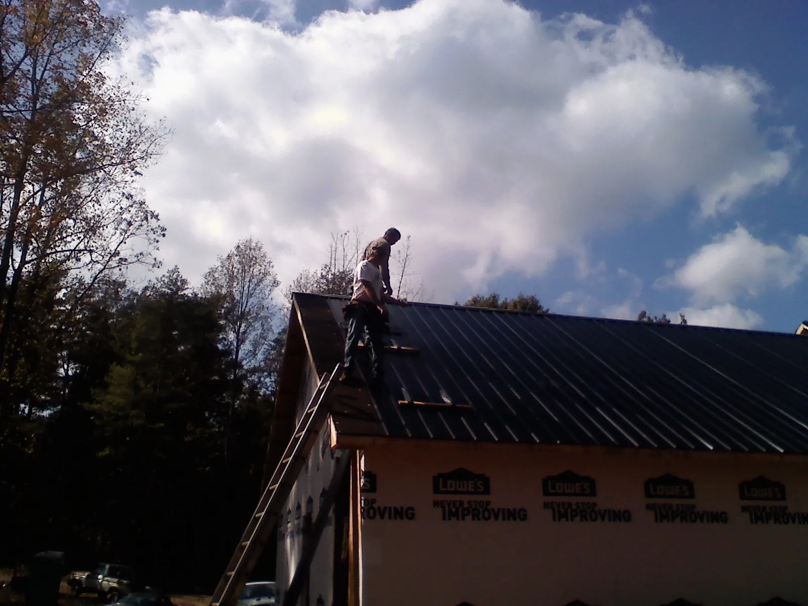 Roofer fastening dark metal panels high against a cloudy sky, from a Roof Inspection job in Harlem