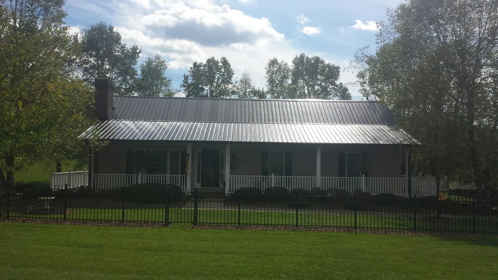 Gray metal roof on a brick ranch with a full width front porch — Gutter Guard Installation work by our crew in Harlem
