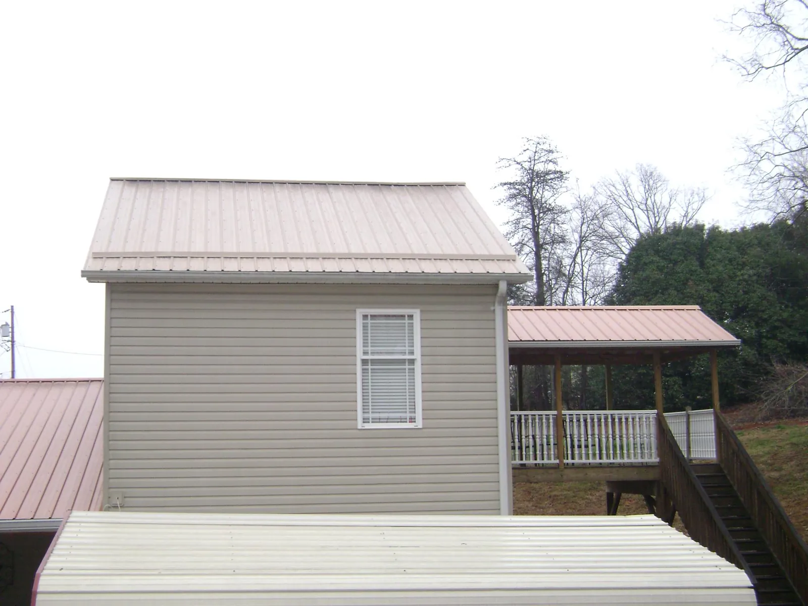 Tan metal roofs on a two story addition and attached porch, from a Roof Replacement job in Harlem